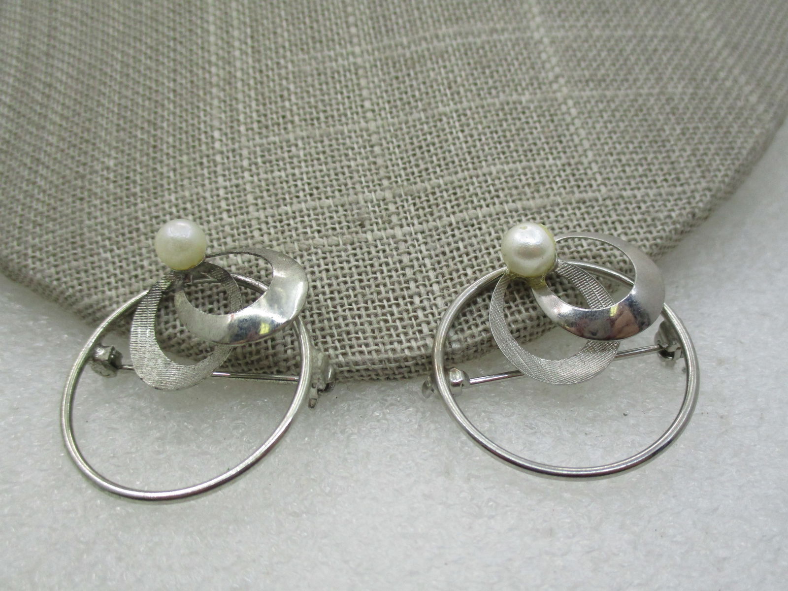 Vintage Pair Faux Pearl Circle Brooches, 1-1/8": Vintage Pair Faux Pearl Circle Brooches, 1-1/8", 1960's, silver plated with a circle and a textured and smooth loop and a faux pearl appx. 5mm. Age is 1960's. Modern design. Not signed by the maker. V