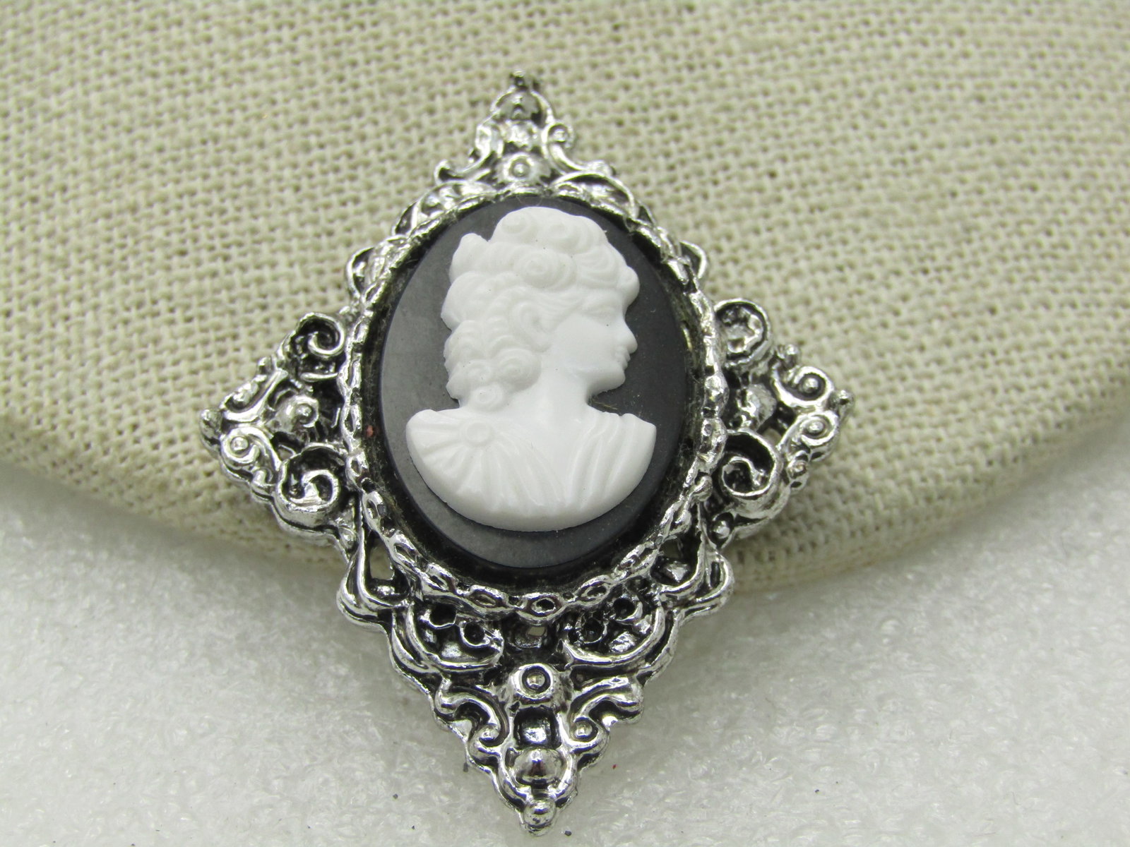 Vintage Black & White Pointed Cameo Brooch, Silver Tone, 2": Vintage Black & White Pointed Cameo Brooch, Silver Tone, 2" by 1.5", 1960's. Diamond shaped scrolled base with a raised oval back background and white plastic pressed cameo. Not signed by the maker. V