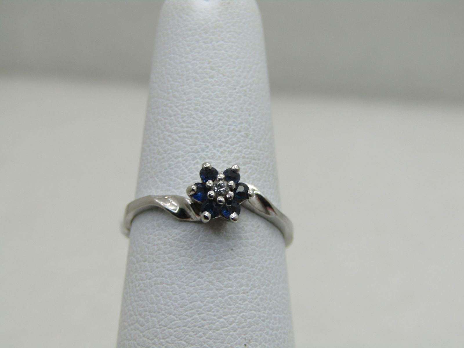 Vintage 10kt Sapphire Diamond Blossom Ring, Sz. 6, Signed: Vintage 10kt Sapphire Diamond Blossom Ring, Sz. 6, Appx, 1,34 grams. Signed, signed pd. White Gold. Six dark blue sapphires that are appx. 1.3mm to 1.5mm wide with a centr diamond raised slightly abov