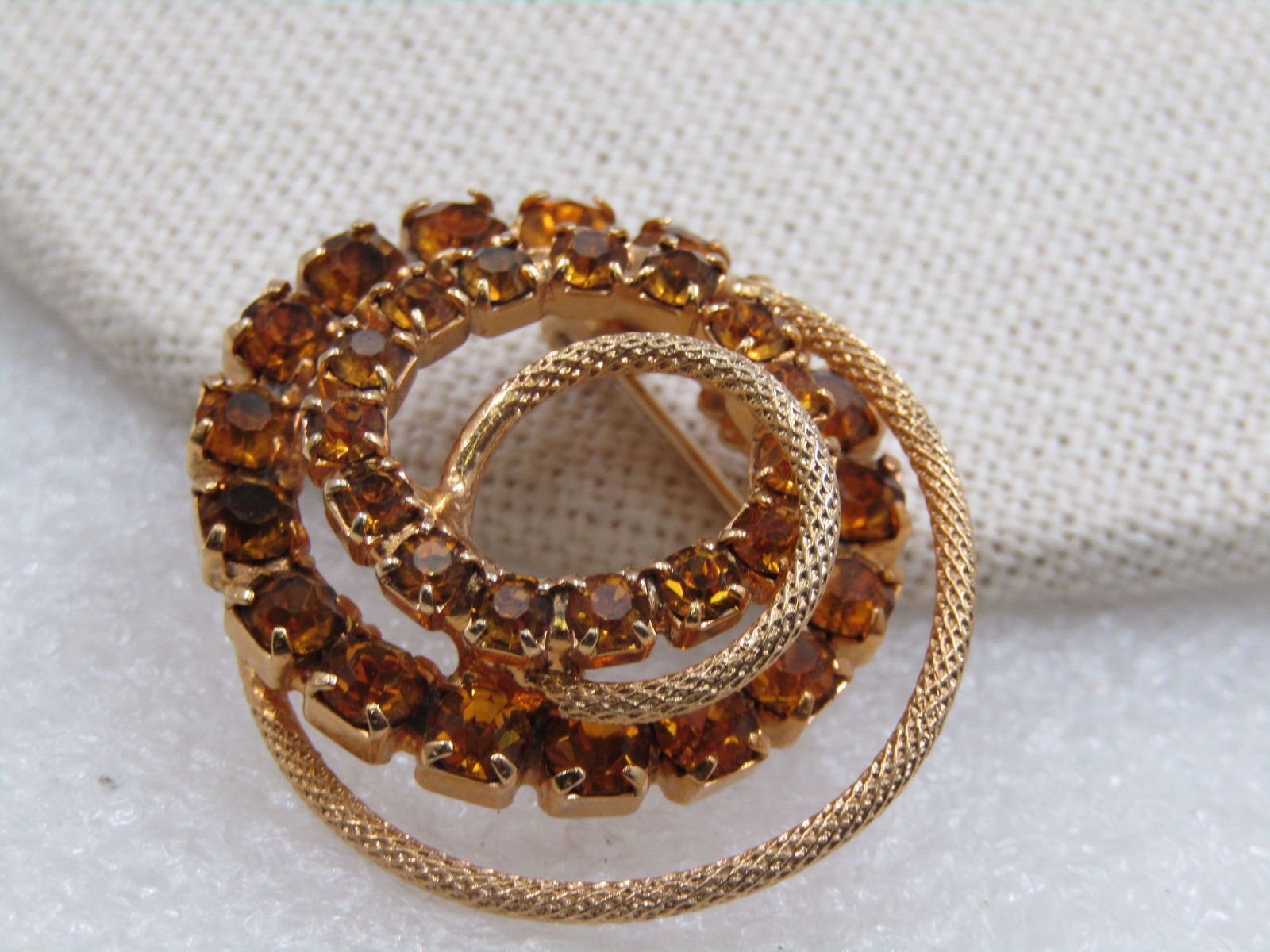 Vintage Golden Rhinestone Spiral Brooch, 1.25", 1960's: Vintage Golden Rhinestone Spiral Brooch, 1-3/8", 1960's. Spiral circle of graduated golden round rhienstones with a textured spiral that gives the brooch an oval shape at 1-3/8". Very good condition.