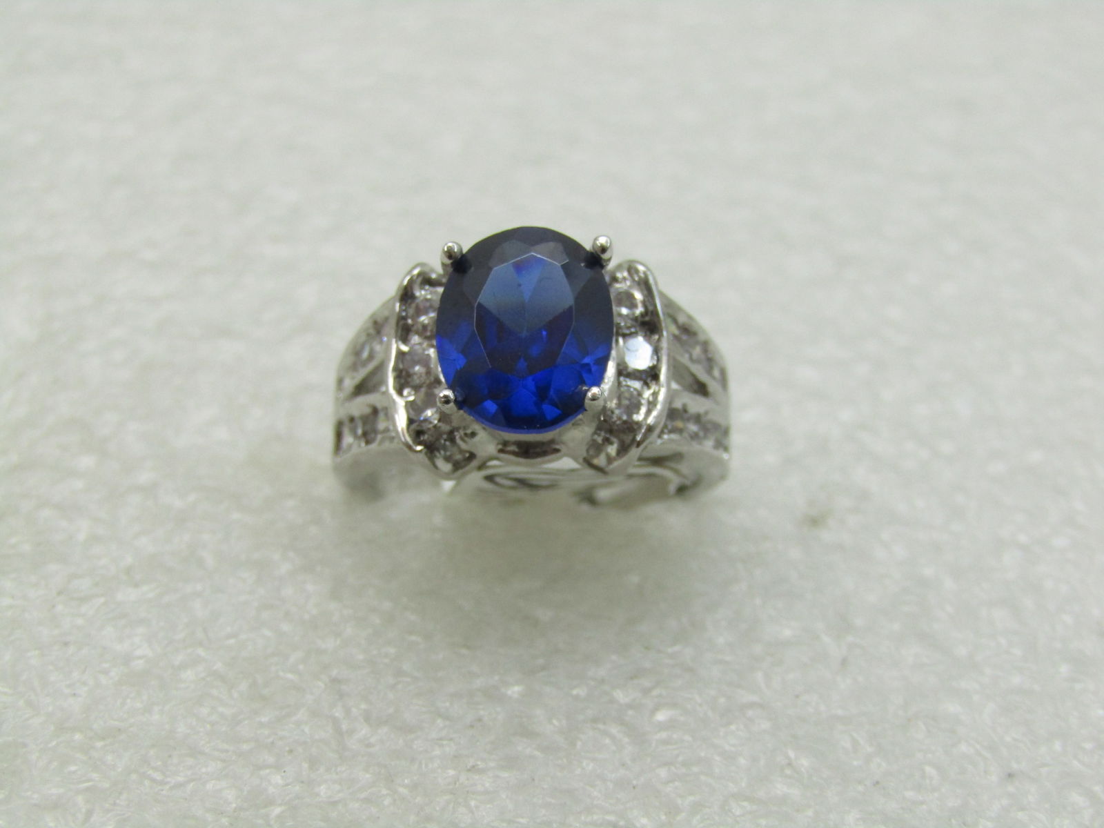 Simulated Blue Sapphire Ring with Clear CZ, Sz. 9.5: Simulated Blue Sapphire Ring, 9.5mm by 7.5mm deep blue stone, CZ/crystal - simulating blue sapphire, with pave set clear simulated diamond accents down the split band and framing the base of the blue