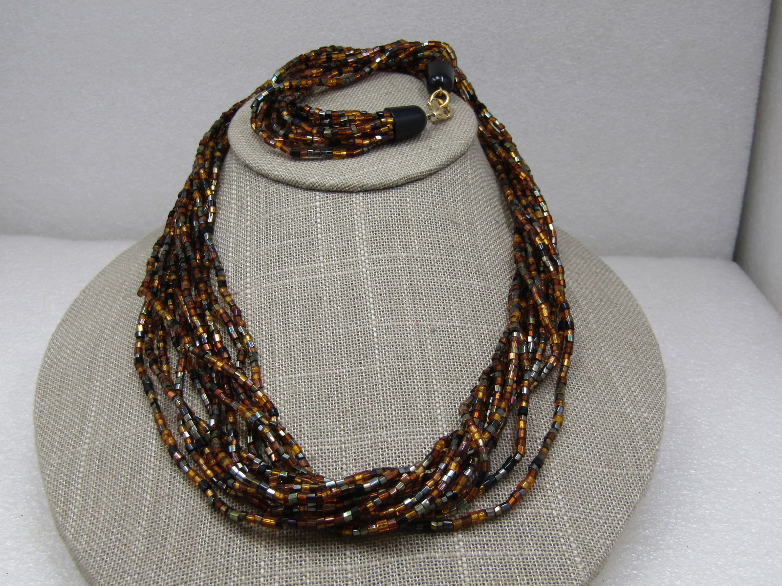 Vintage Black & Amber Torsade Multi-Strand Necklace, 12 Strands, 25": Vintage Black & Amber Torsade Multi-Strand Necklace, 12 Strands, 25". Very complimentary glass seed beads in amber, black, gold, brown mixed throughout the strands. Black Plastic rounded encaps and a