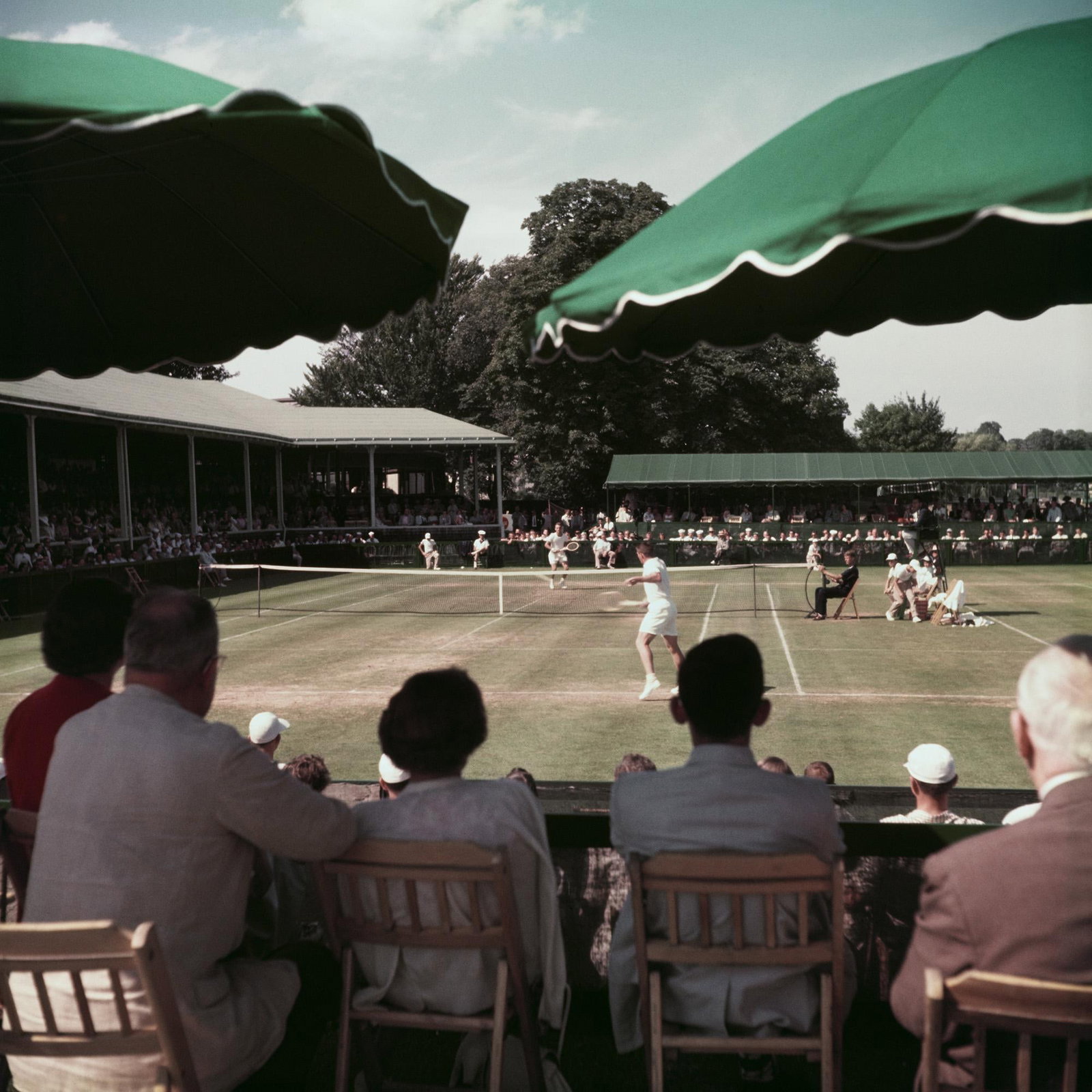 Tennis At Newport Casino Slim Aarons Limited Estate Stamped Edition: 1953 (Printed Later): Title: Tennis At Newport Casino Slim Aarons Limited Estate Stamped Edition: 1953 (Printed Later) Description: A view from the umbrella boxes towards the tennis court at Newport Casino, Newport, Rhode