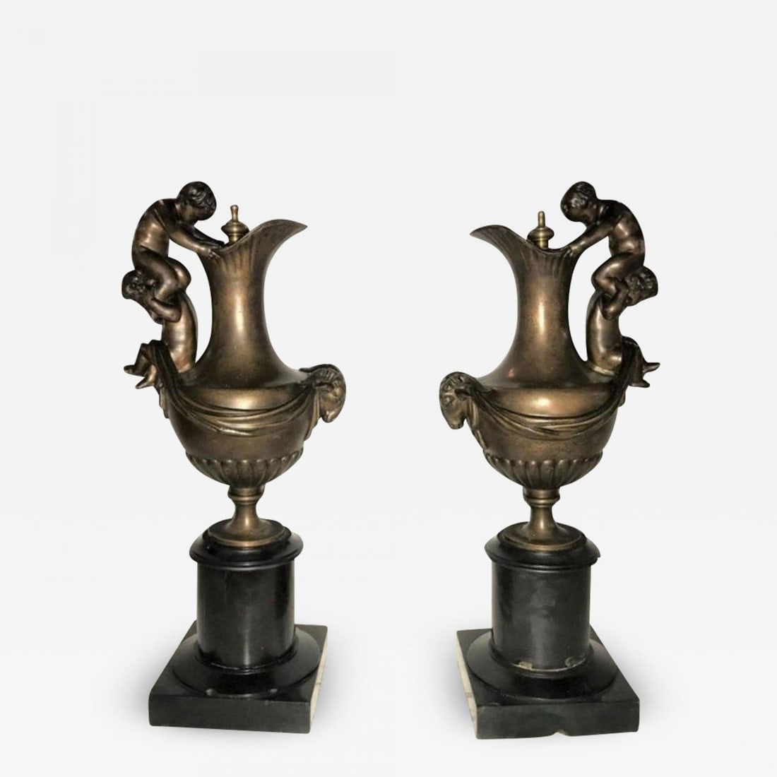 Pair of 19th Century Urns on Marble Stands Bearing Cherubs and Rams Heads: Pair of 19th century French urns on marble stands bearing cherubs and rams heads. Each of these finely chased and bronze patinated urns or water pictures were previously mounted as table lamps and can