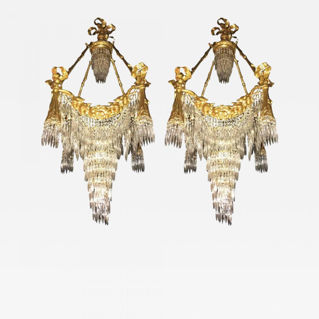 Pair of Bronze Louis XVI Style Crystal Ribbon and Tassle Drapery Chandeliers: A pair of Bronze Louis XVI style crystal ribbon and tassle drapery chandeliers with 18 lights. Each newly wired. This fine custom quality pair of chandeliers are simply stunning and are certain to lig
