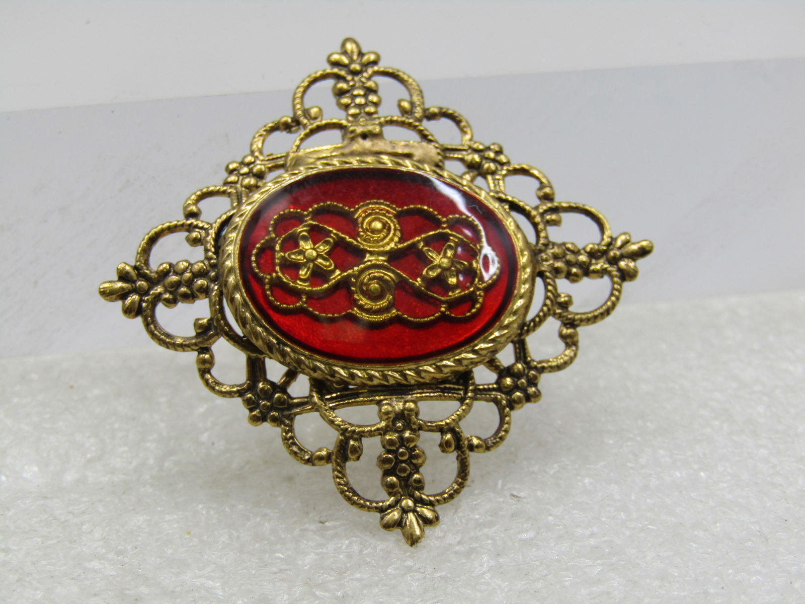 Vintage Red Filigree Scrolled Brooch, Mid-Century, 1.25" Square: Vintage Red Filigree Scrolled Brooch, Mid-Century, 1.25" Square. Gold tone square set on the points that have a fleur-de-lis style tip. The center has a framed red plastic oval that is 1" wide and 3/4