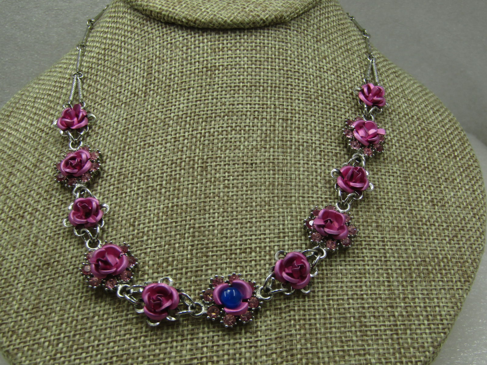 Vintage Pink Metallic Rose Necklace, 17", Pink Rhinestones & Blue Stone, Avon: Vintage Pink Metallic Rose Necklace, 17", Blue Stone, Avon. Avon necklace fromt he 1980's with pink metalic rose blossom with 11 total roses - the center rose had a retro fit in that there is a blue r