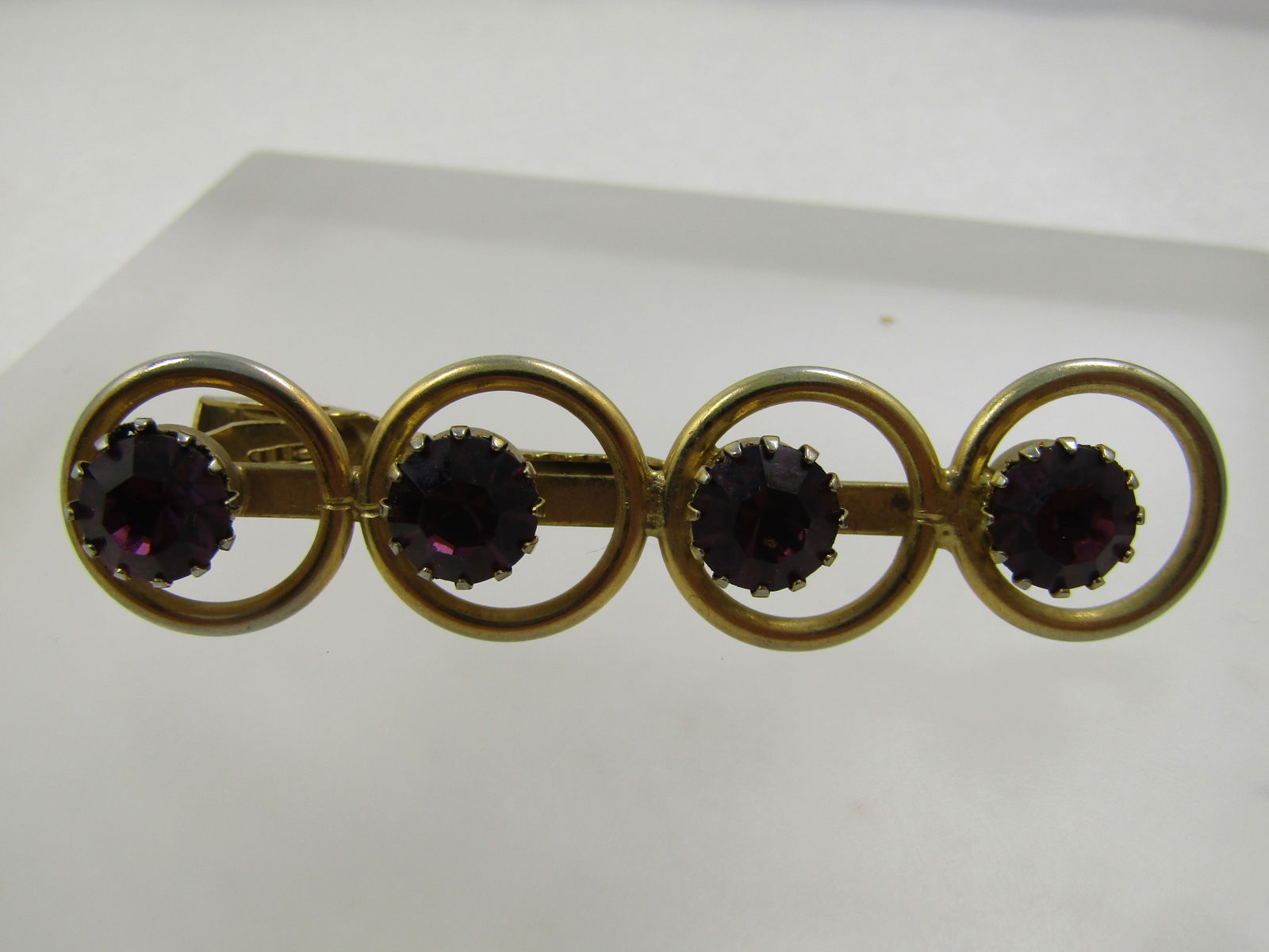 Vintage Purple Rhinestone Tie Clasp, 1960's: Vintage Purple Rhinestone Tie Clasp, 1960's. Gold tone with four circles over the clasp each with an appx. 8.5mm round purple glass rhinestones set with prongs all the way around it and set to the lef
