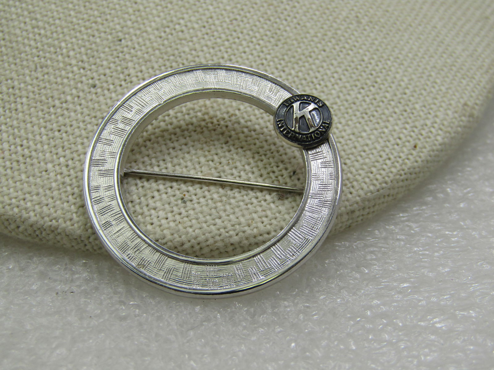 Vintage Kiwanis International Circle Brooch, 1.25", 1960's: Vintage Kiwanis International Circle Brooch, 1.25", 1960's. It has a textured design around the center of the circle with a raised smooth edge and a 7mm round Kiwania International Logo set on the cir