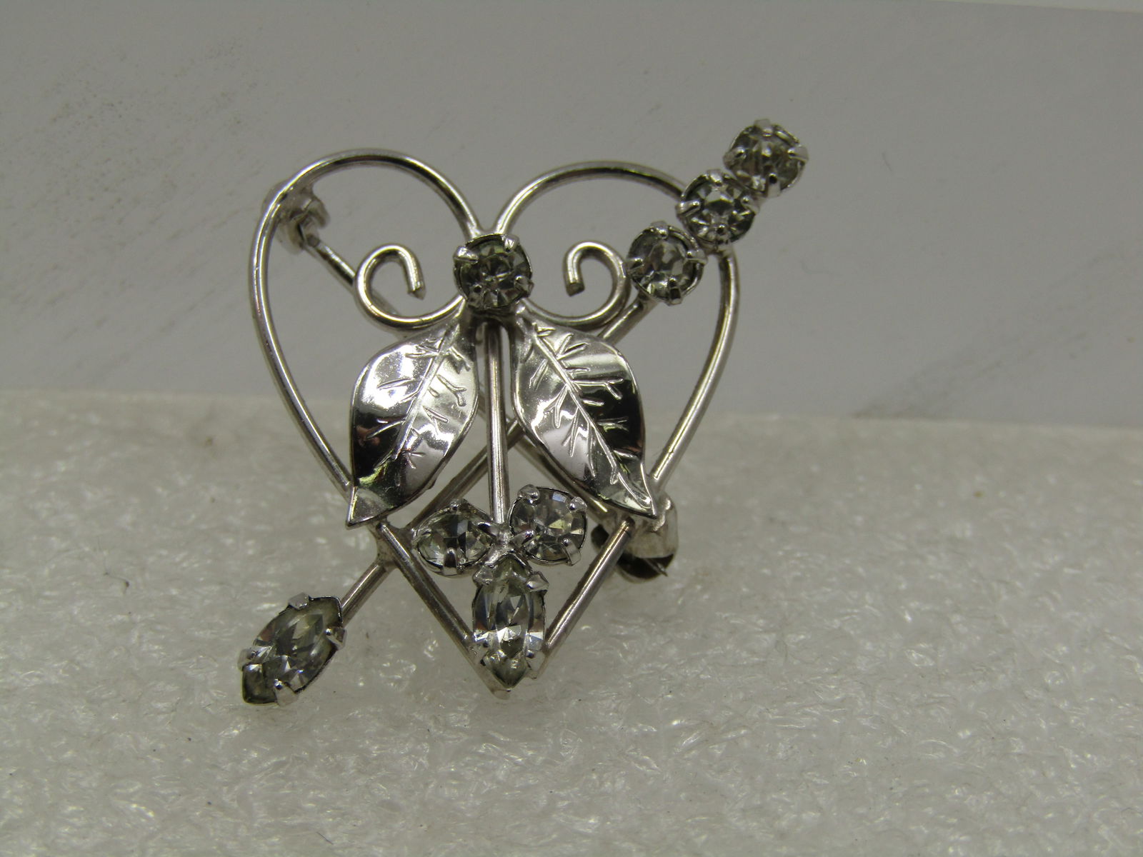 Vintage Sterling Heart Rhinestone Brooch, Signed D'Or, 1960's: Vintage Serling Heart Rhinestone Brooch, Signed D'Or, 1960's. 1.25" long and 1" wide. It is an open heart with scrolled and leaf accents and a rhinestone arrow crossing through it with other