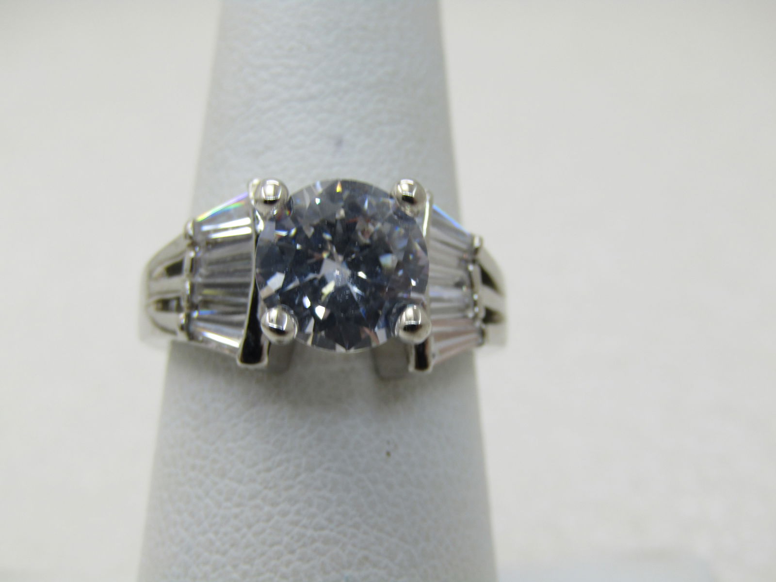 Silver Tone Tiered CZ Engagement Ring, Sz. 7.5, 2TCW Main Stone with Baguettes: Silver Tone Tiered CZ Engagement Ring, Sz. 7.5, 2.10 TCW Main Stone with Baguettes. The main stone is held with four prongs and a stepped down design with three baguettes in each side with an open des