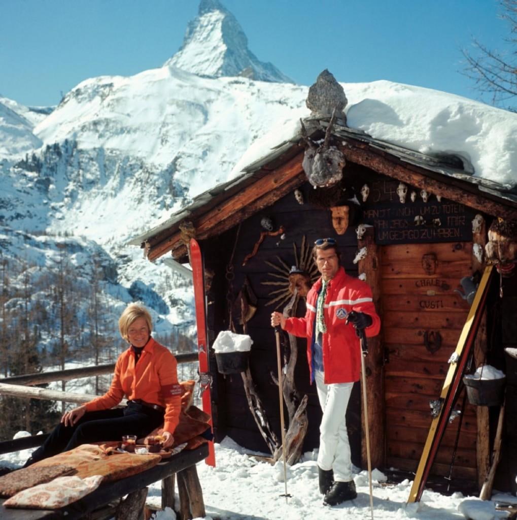 Slim Aarons Official Estate Print - Chalet Costi - Oversize: 1968 (Printed later): Title: Slim Aarons Official Estate Print - Chalet Costi - Oversize: 1968 (Printed later) Description: Chalet Costi Skiers outside the Chalet Costi in Zermatt, 1968. Paper size 48 x 48" / 122 x 122 cm