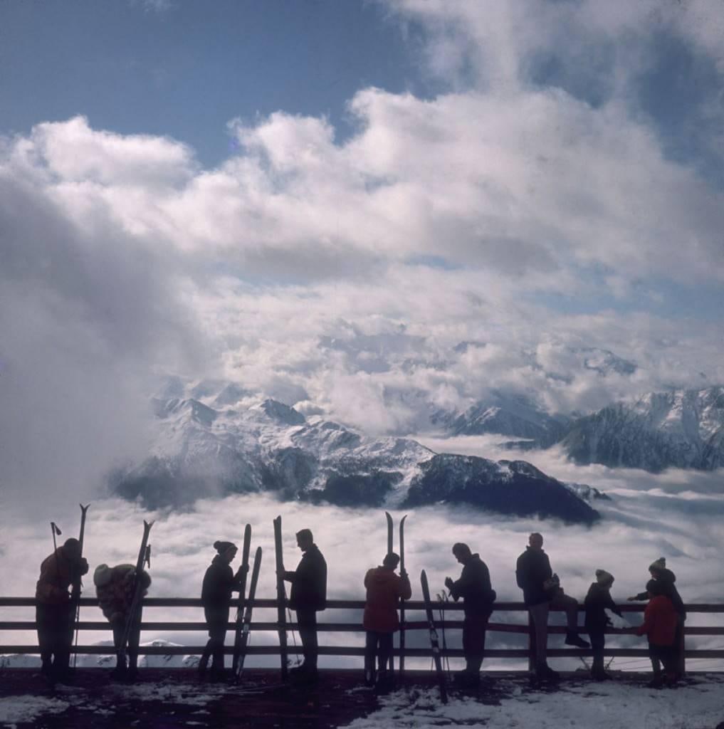 Slim Aarons 'Verbier View' Official Limited Estate Edition: 1964 (Printed Later): Title: Slim Aarons 'Verbier View' Official Limited Estate Edition: 1964 (Printed Later) Description: Verbier View' Skiers admire the view across a valley of clouds at Verbier, 1964. Paper size 48 x