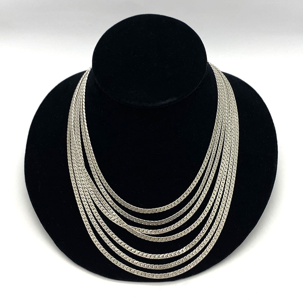 Monet Multi-Strand Necklace: This is a Monet multi-strand chain necklace. This 1980s vintage necklace comes with seven strands of 0.125" width silver-tone metal chains and a Monet rectangle tag. The measurement from shortest