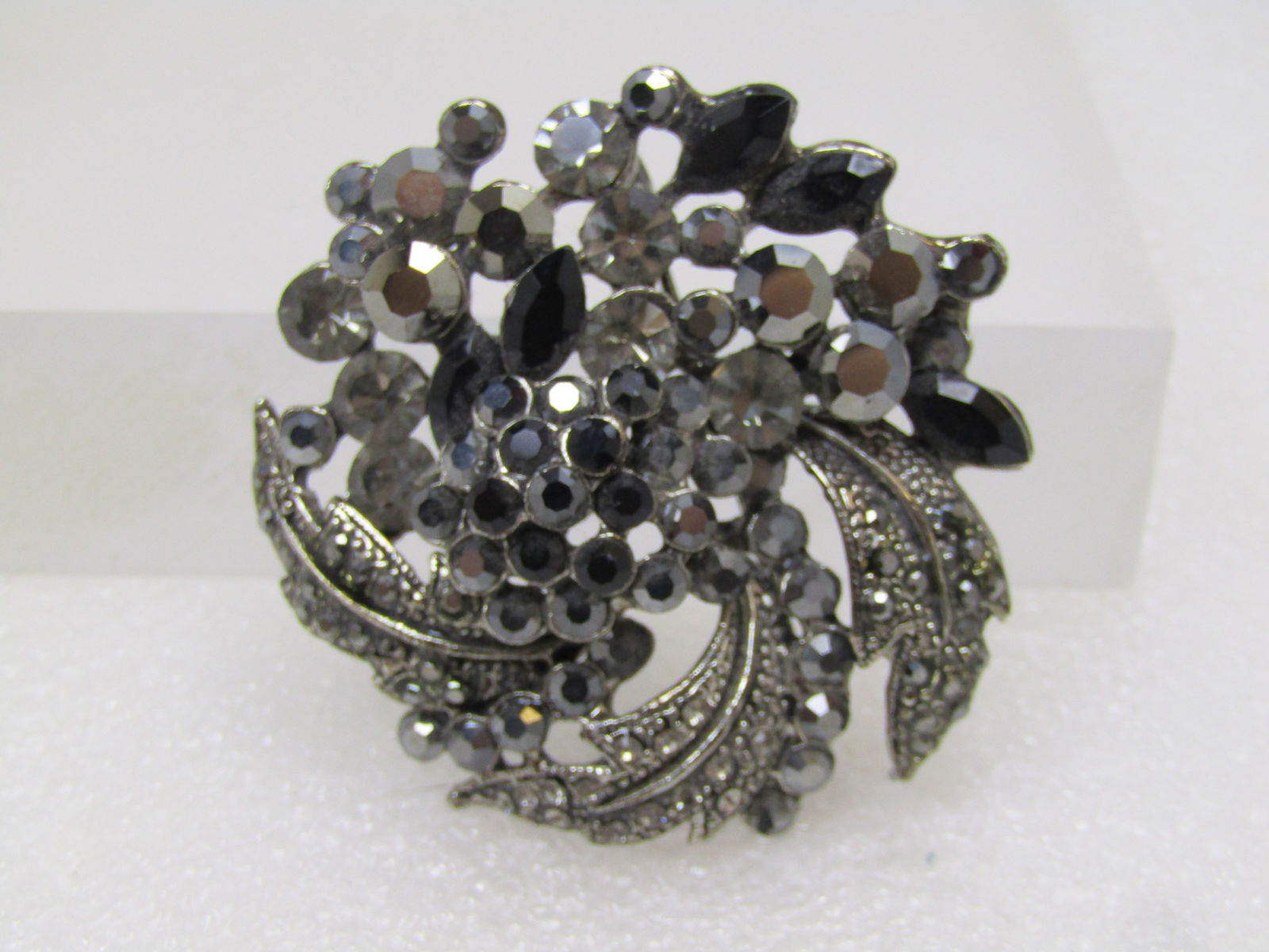 Black & Gray Rhinestone Floral Brooch, Silver and Black Tone Metal, 1980's-1990's: Black & Gray Rhinestone Floral Brooch, Silver and Black Tone Metal, 1980's-1990's. This has a blossom design with raised black stones in the center and silver tone curved leaves with black and gray