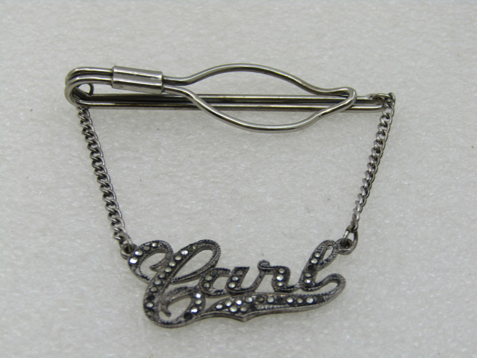 Vintage Sterling Marcasite Carl Name Tie Bar, 1940's-1950's, 2.5": and 2.75" long. Carl in sterling with sterling chain and encrusted with marcasites in the name and scroll. There is one damaged marcasite and one that is in upside down. Photo will show missing