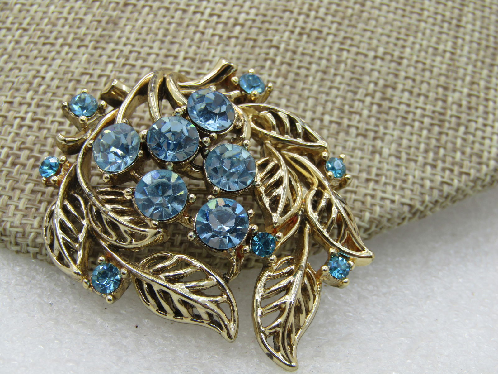 Vintage Blue Rhinestone Floral Swag Brooch, 2", Gold Tone, 1960's: Vintage Blue Rhinestone Floral Swag Brooch, 2" tall and 1.75" wide, Gold Tone, 1960's. Open leaves make up the cascading swag with a cluster of larger blue rhinestones making up the blossoms. Not sign