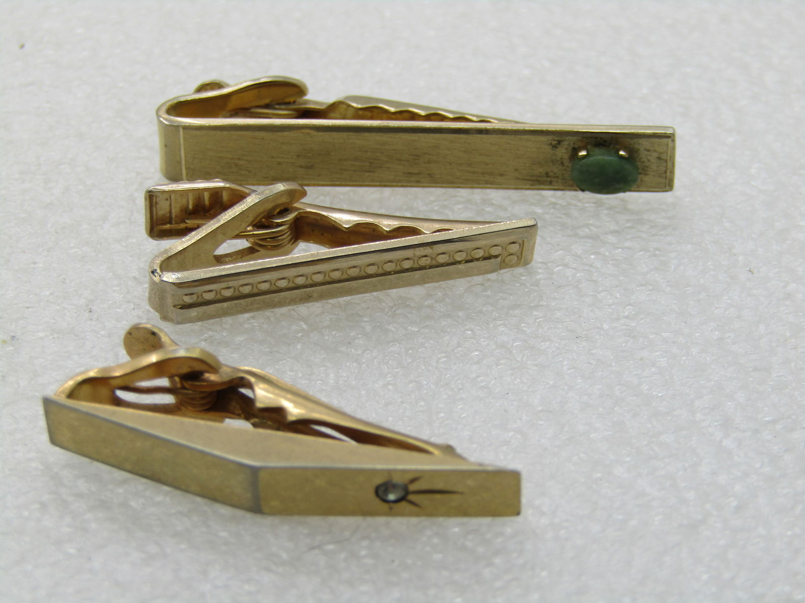 Vintage 3 Tie Clasp Lot, 1960's Gold Tone, Swank, Dante: Vintage 3 Tie Clasp Lot, 1960's Gold Tone, one with a green stone signed Dante; a Swank with a clear stone and peaked center that is 1.5" long; and one unsigned art deco design that is appx. 1.25".