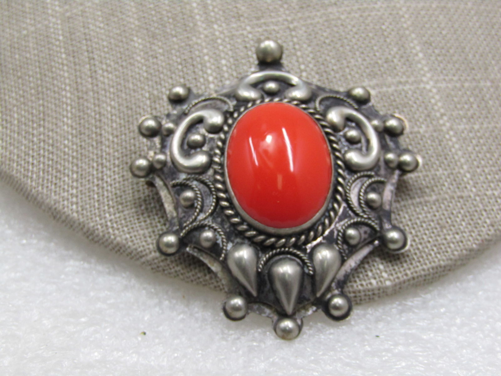 Vintage Orange Stoned Bali Brooch, 2.5": Vintage Orange Stoned Bali Brooch, 2.5" by 1.5". 1" oval orange acrylic cabochon bezel-set with repousse teardrop and scrolled accents and thin rope accents and wide rope accent around the stone with