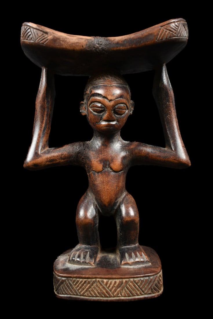 Neck rest – Wood – Luba – Congo DRC: A beautiful LUBA neck rest, D.R. Congo. It has a detailed figure with intricately carved face; beautiful patina. The wooden neck rest is widely used by women to protect their hairdo. When they lie on