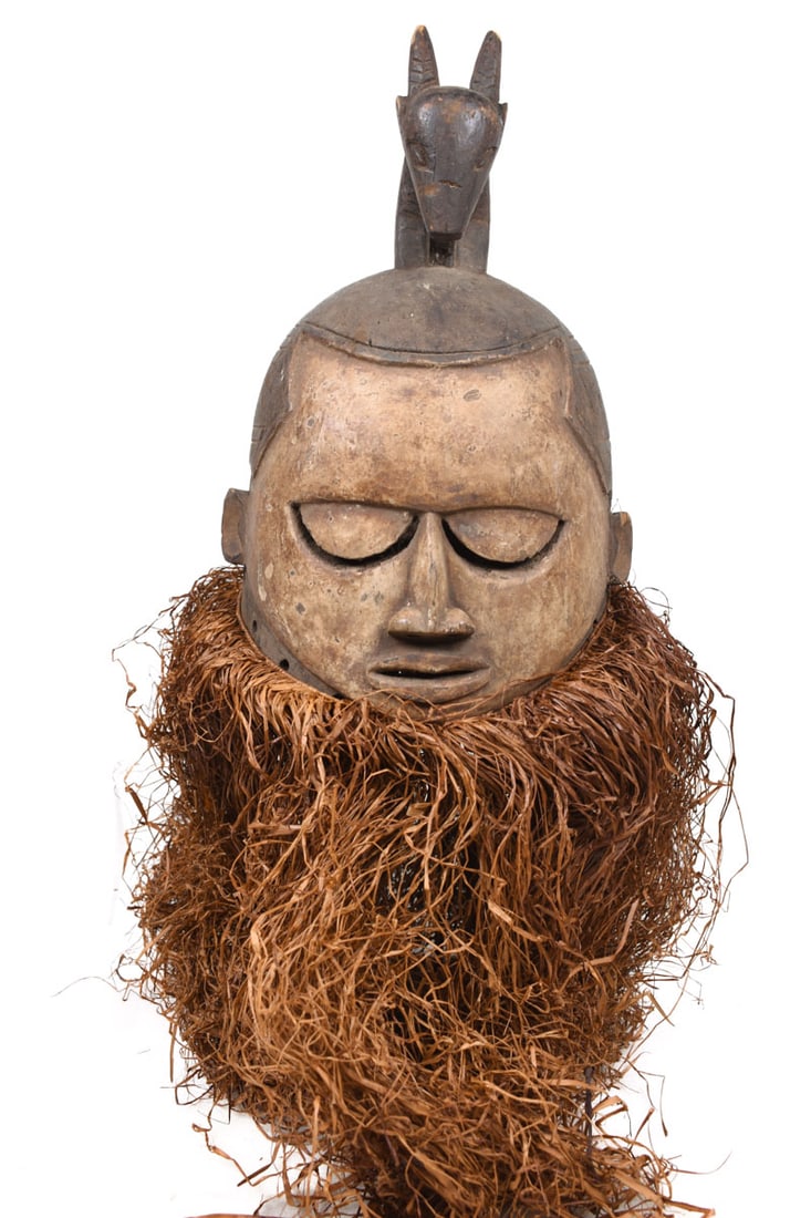 Helmet Mask – Wood, Raphia – Suku – Congo: Worn during male initiation ceremonies, masks like these represented all departed ancestors. Mourning songs were sung during the ritual; the vertical lines on the face are tears. Neighbors of the Yaka