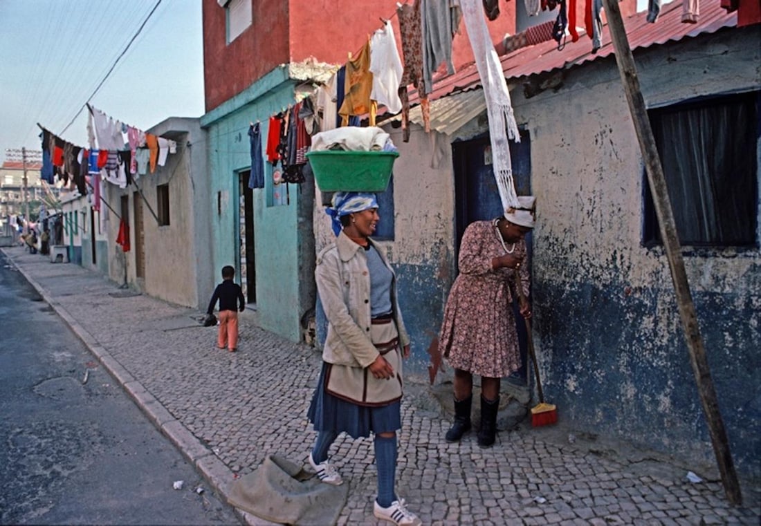 Walk On By by Alain Le Garsmeur: 1984 (printed later): Title: Walk On By by Alain Le Garsmeur: 1984 (printed later) Description: Walk On By by Alain Le Garsmeur A Cape Verde immigrant woman carrying a wash basket on her head walks by a neighbour cleaning