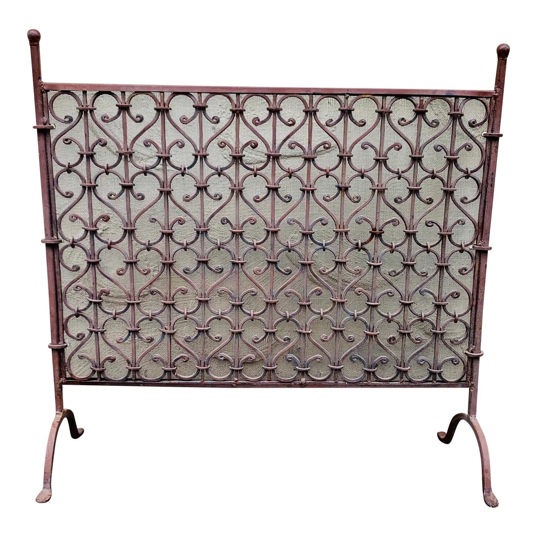 Antique Late 19th Century Spanish Wrought Iron Fireplace Screen: American wrought iron free standing fire screen with flanking ball finials, decorative scrolled centered panel with interior lined mesh, tapered supporting columns, and terminating on scrolled legs wi