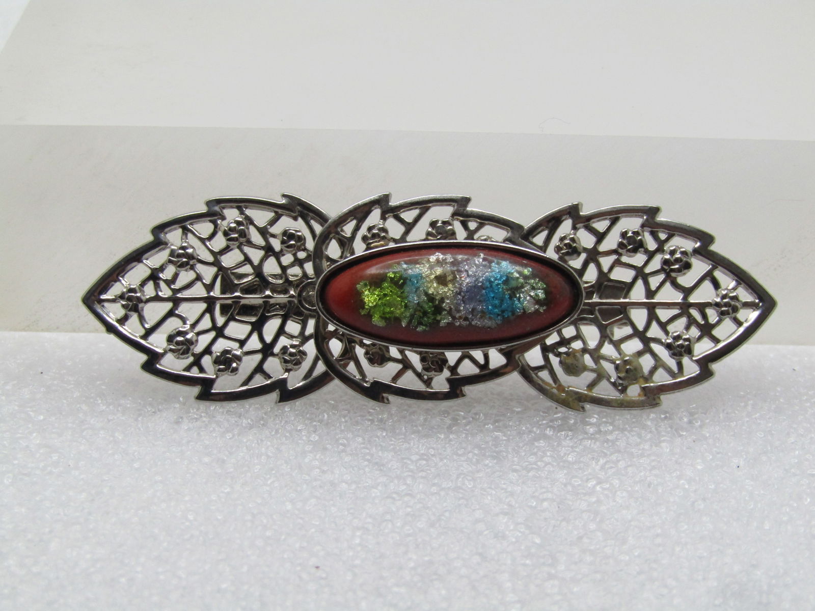 Vintage Filigree Leaf with Glitter Stone Brooch, 1960's-1970's: Vintage Filigree Leaf with Glitter Stone Brooch, 1960's-1970's. Silver tone filigree designed leaves with an oval brown stone with pastel glittery accents on top with clear finish laminate on top. The