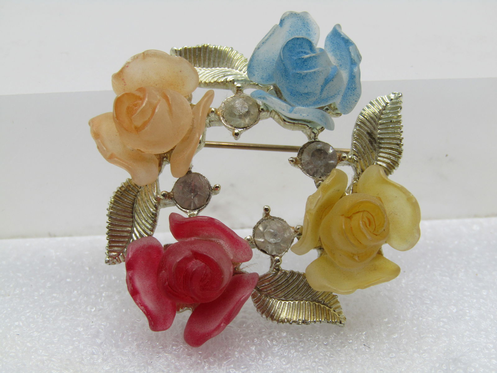 Vintage Faux Carved Rose Brooch with Rhinestones, 1950's-1960's: Vintage Faux Carved Rose Brooch with Rhinestones, 1950's-1960's. Gold tone open center brooch with a setting of textured leaves with a yellow, pale orange, red, and aqua faux carved rose blossom sitti