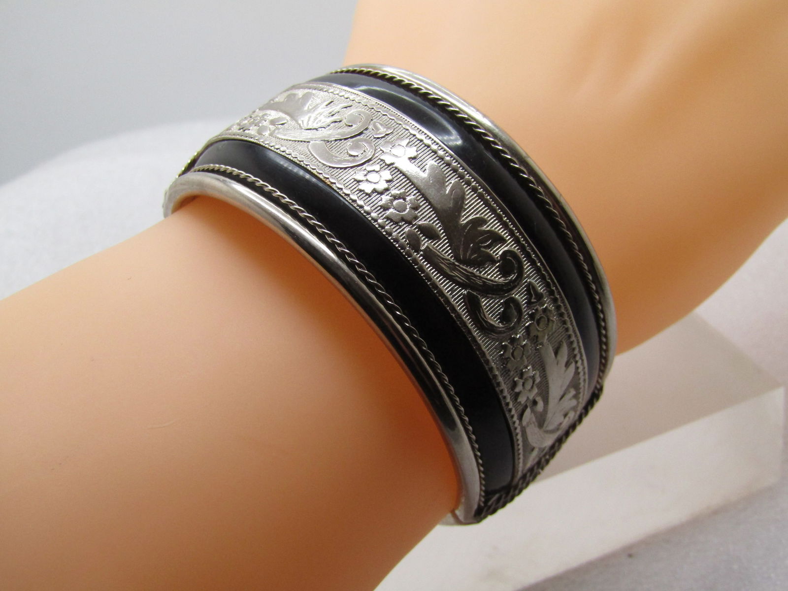 Vintage Black Enameled & Floral Cuff Bracelet, Hinged, 7" 1960's-1970's: Vintage Black Enameled & Floral Cuff Bracelet, Hinged, 7" 1960's-1970's. It is appx. 1.25" wide. It has a silver tone main setting with rounded edges and rope accents on the inside of that with a cent