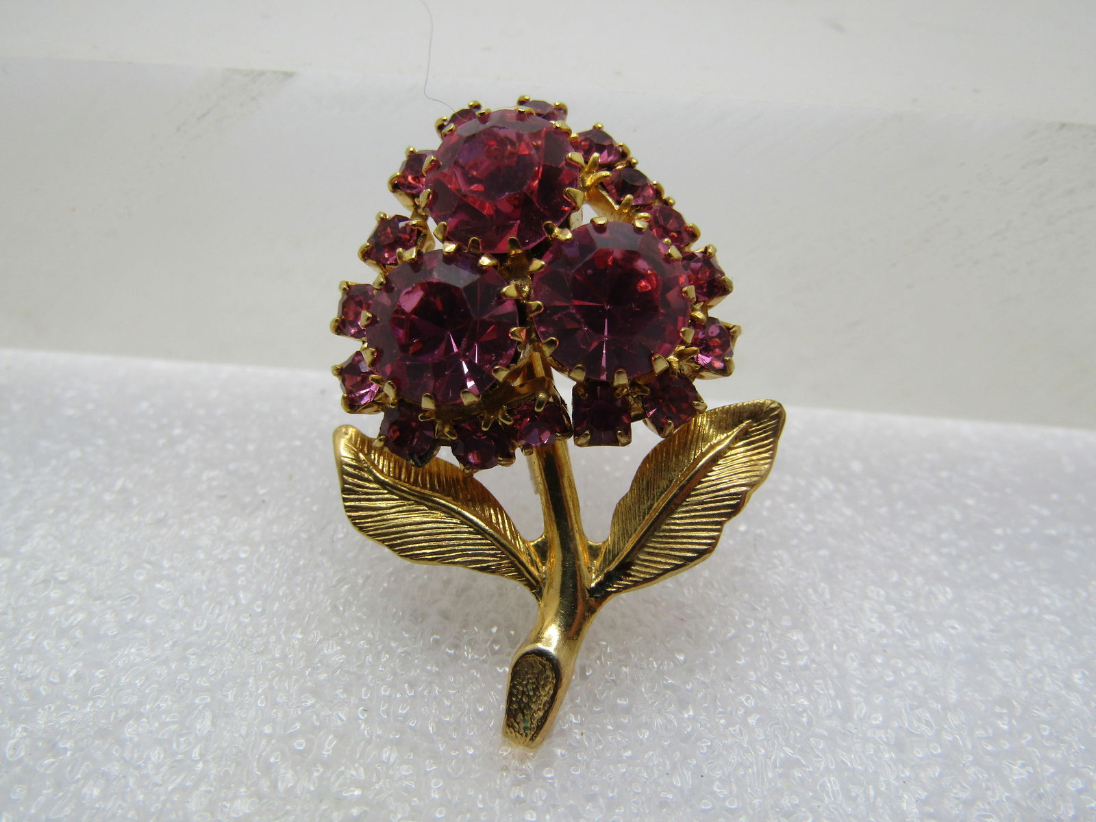 Vintage Pink Rhinestone Floral Brooch, Blossom & Stem, 1960's: Vintage Pink Rhinestone Floral Brooch, Blossom & Stem, 1960's. Gold tone with textured leaves and smooth stem. It has three large pink 8.5mm round s tones that are prong-set and sit higher on the sett