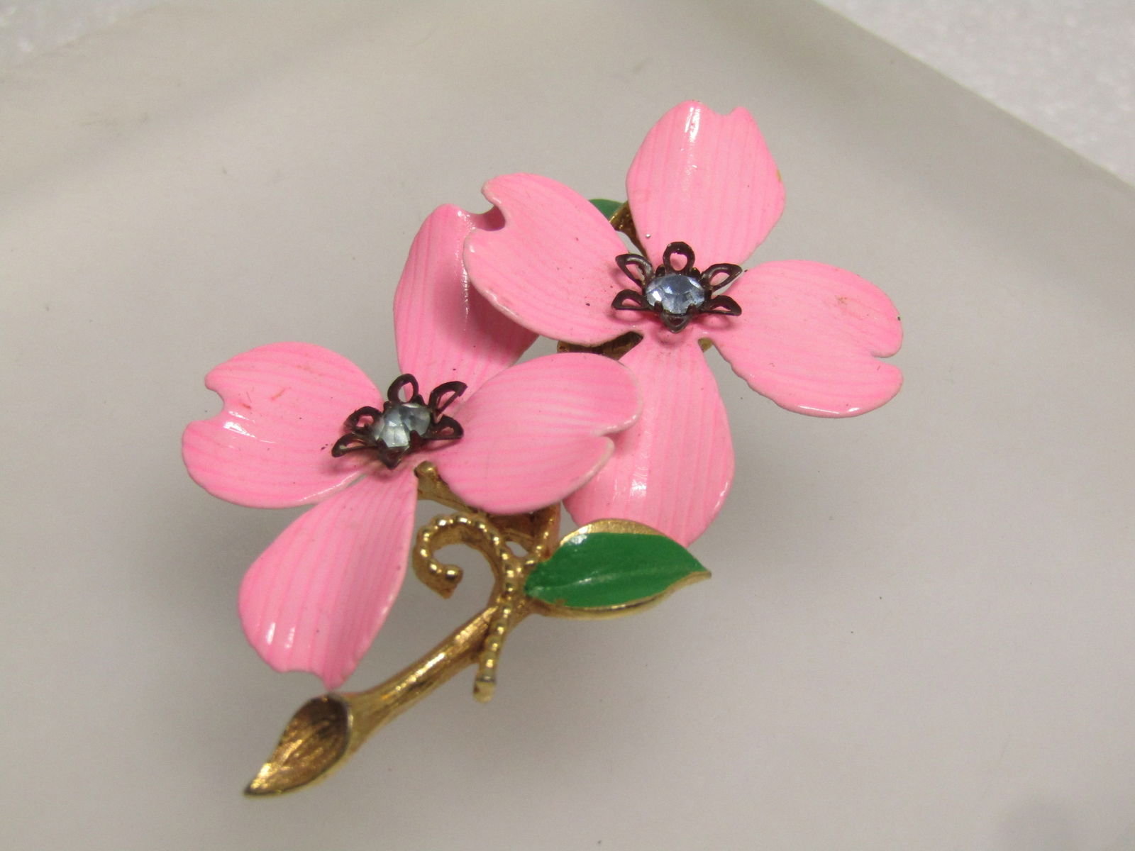 Vintage Pink Double Dogwood Brooch, Rhinestones, 1960's: Vintage Pink Double Dogwood Brooch, Rhinestones, 1960's. Two pink dogwood blossoms on a gold tone stem with green enameled leaves. The petals are slightly ridges and enameled pink with a black pointed