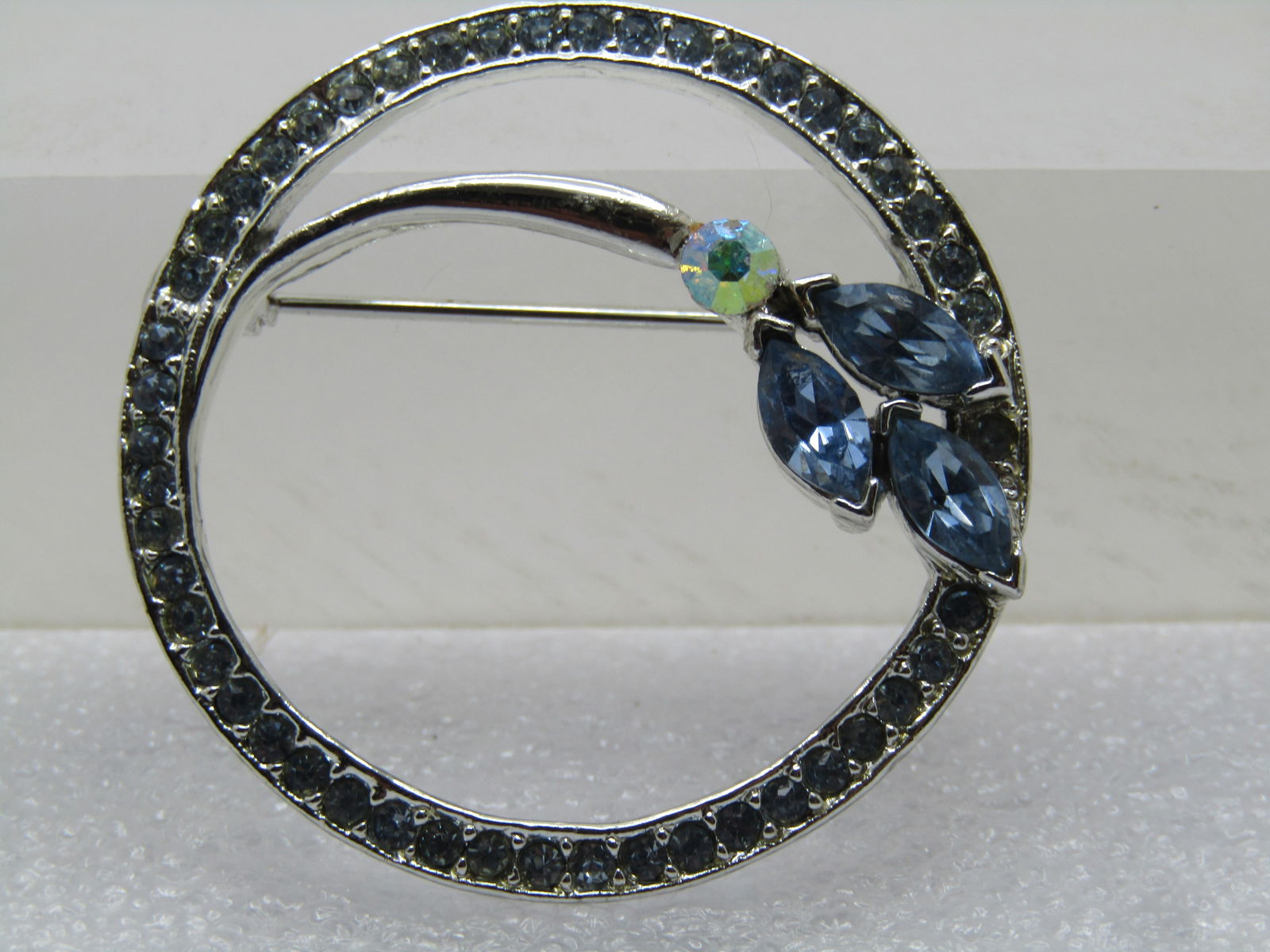 Vintage Baby Blue Rhinestone Floral Brooch, Circle, , 1970's-1980's: Vintage Baby Blue Rhinestone Floral Brooch, Circle, , 1970's-1980's. Silver tone with baby blue rhinestones set in the appx. 3.5mm wide circle frame with a curved floral stem/marquise blossom on the l