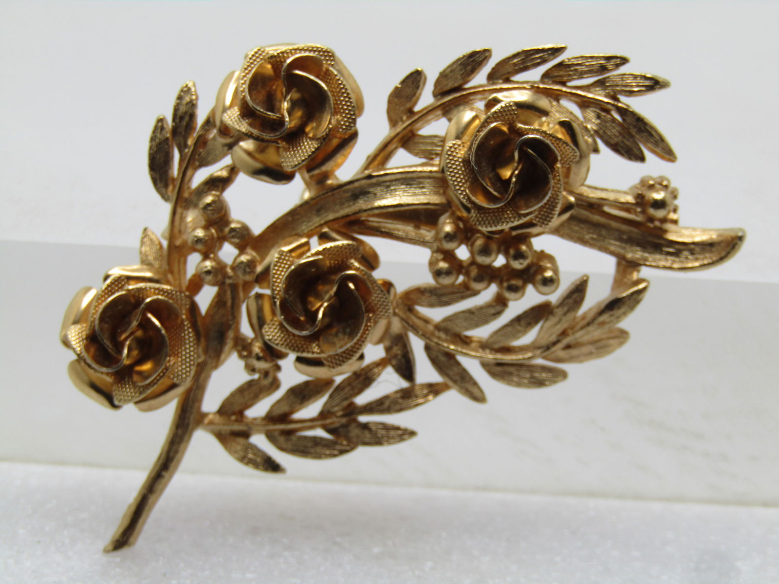 Vintage Coro Floral Blossom Stem Brooch, 1960's: Vintage Coro Floral Blossom Stem Brooch, 1960's. Gold tone and appx. 2.5" tall and 1.75" wide. Four textured blossoms with four leaf stems and other accents - look like roses. One of the leaf blades w