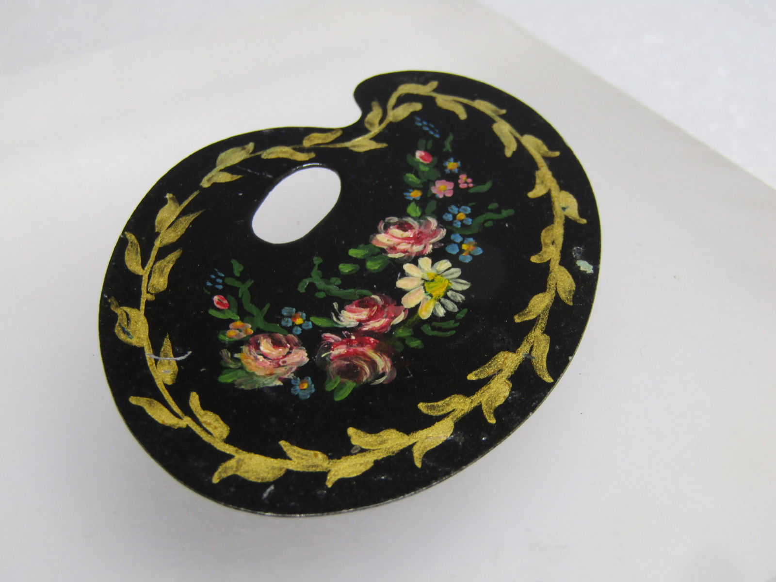 Vintage Floral Painted Palet Brooch, 1960's, Black Enameled: Vintage Floral Painted Palet Brooch, 1960's, Black Enameled. Black enameled palet with gold leaf vine frame and flowers painted in the center. Painted on tin with locking clasp. It is appx. 2" by