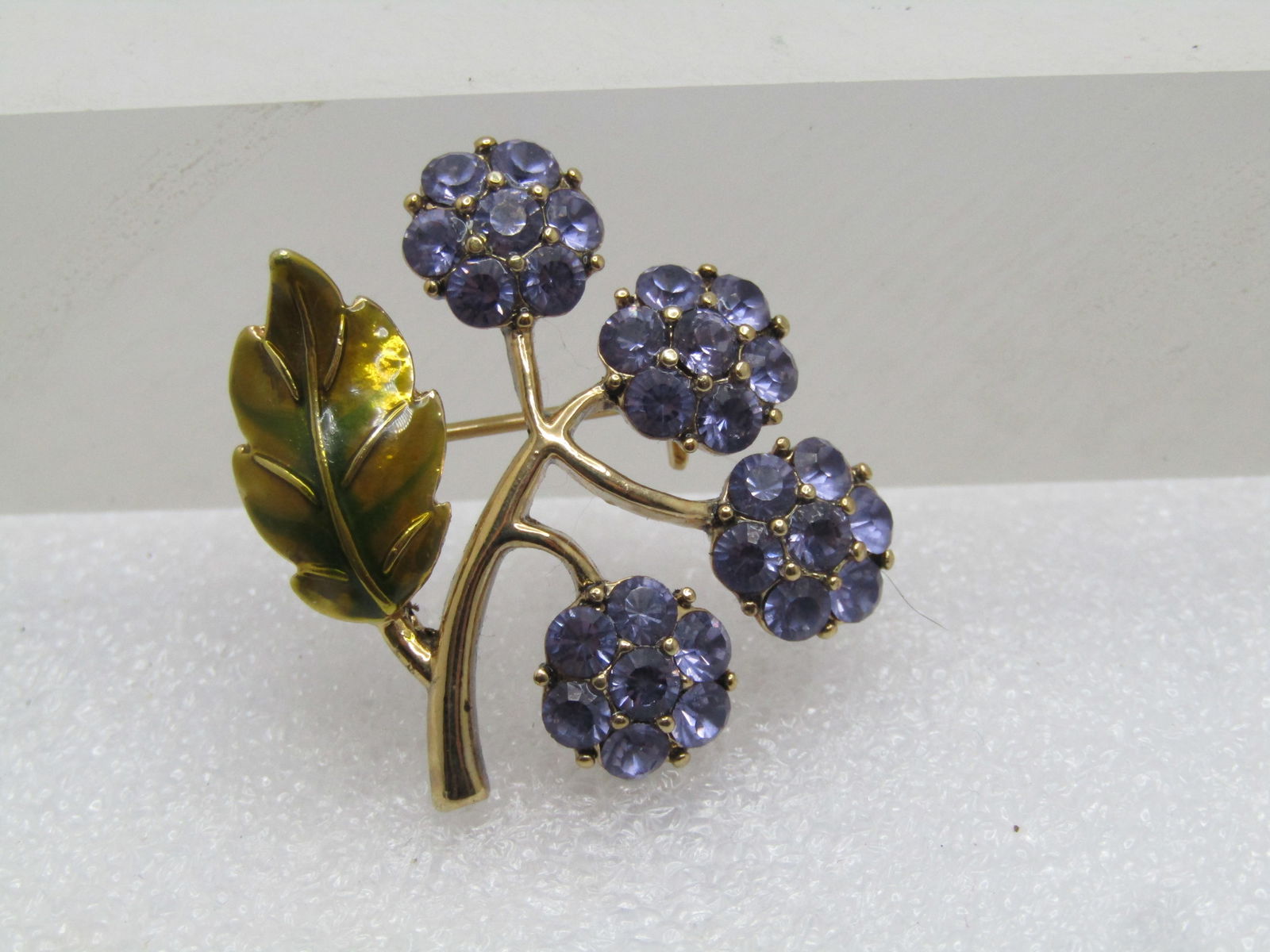 Vintage Purple Enameled Floral Stem Brooch, 1960's: Vintage Purple Enameled Floral Stem Brooch, 1960's. Four purple rhinestone cluster blossoms on a gold tone stem with green enameled leaf. It is appx. 1.25" tall and wide. each blossom is appx 1/3" acr