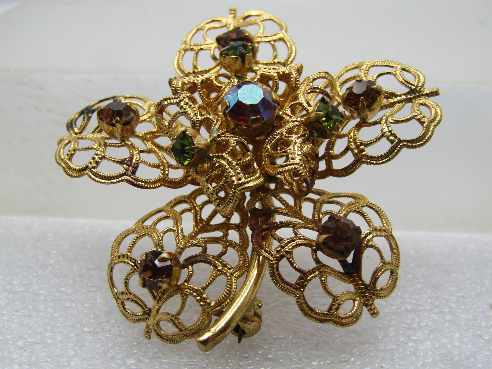Vintage AB Rhinestone Floral Brooch, Filigree, 1960's-1970's: Vintage AB Rhinestone Floral Brooch, Filigree, 1960's-1970's. Peacock aurora borealis colored round stones and green stones. , prong-set on top. Tiered filigree curved petals. Stem is solid and