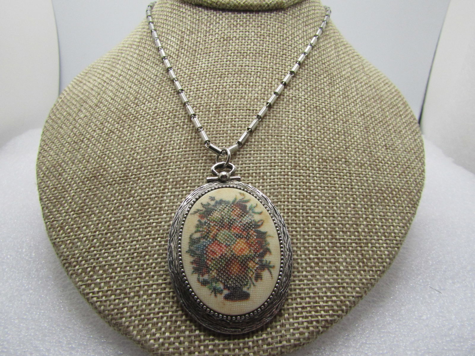 Vintage Faux Sampler Necklace, Sarah Coventry, 1960's, 15": Vintage Faux Sampler Necklace, Sarah Coventry, 1960's, 15". Silver tone frame with a faux needlepoint design of a floral sampler. It has a locket-like look to it. The pendant is appx. 2.25" tall and 1