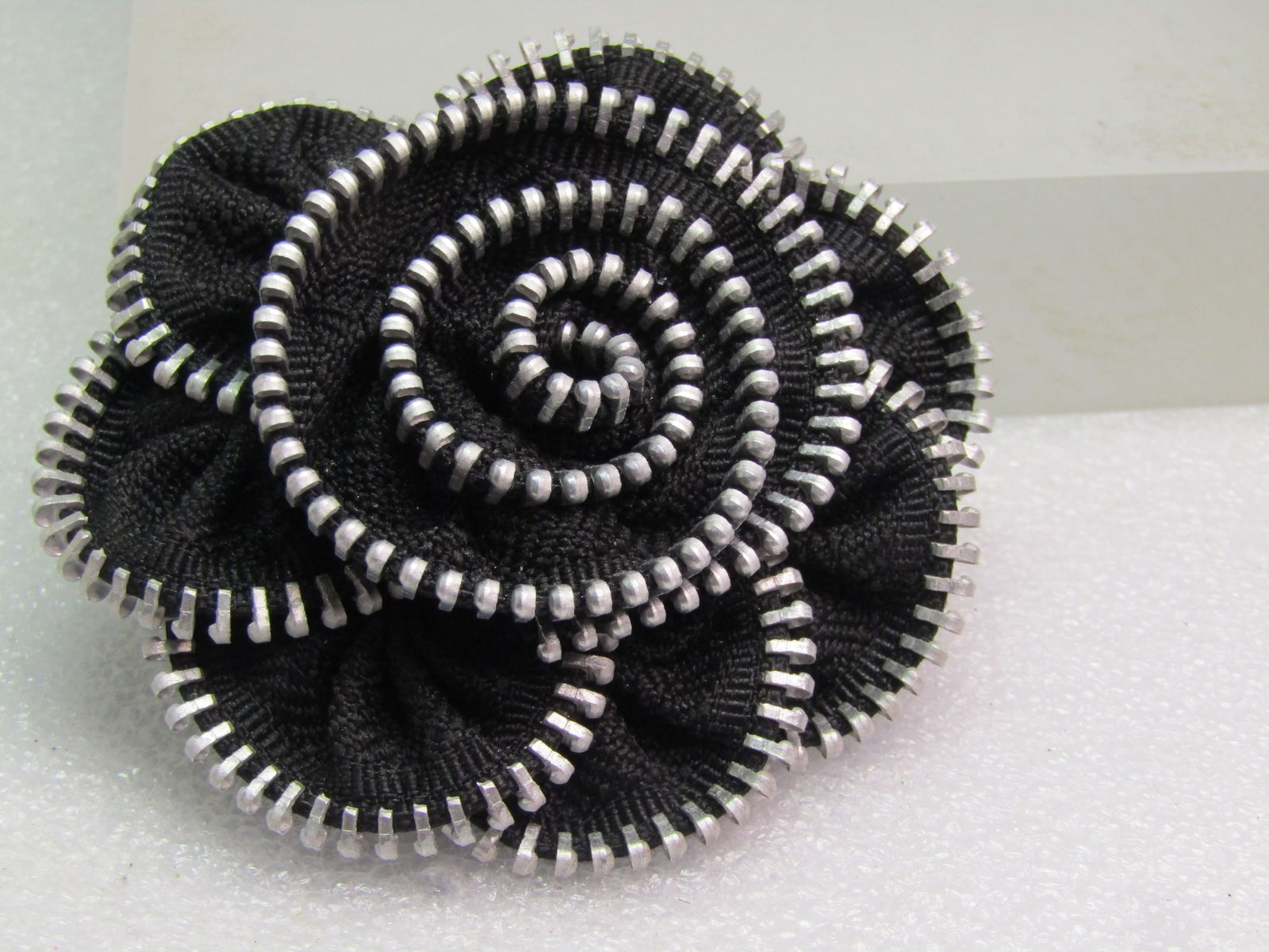 Vintage Zipper Rose Brooch, Black/Silver Tone, 1980's: Vintage Zipper Rose Brooch, Black/Silver Tone, 1980's. This is half of a black zipper with a chunky design. It is appx. 2.75" across with a spiral top tiered and scalloped base tier. Silver tone