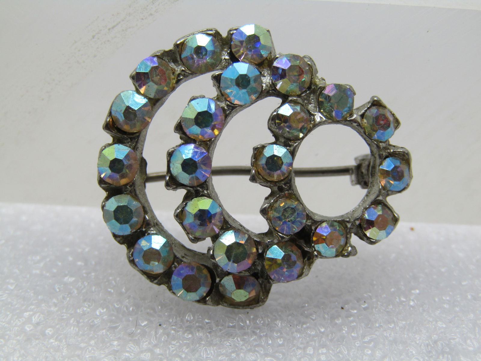 Vintage Aurora Borealis Curved Brooch, 1930's-1940's: Vintage Aurora Borealis Curved Brooch, 1930's-1940's. Silver tone cast metal with a locking clasp. it has a 5/8" circle of pastel/clear aurora borealis stone and two large curved arches off the bottom