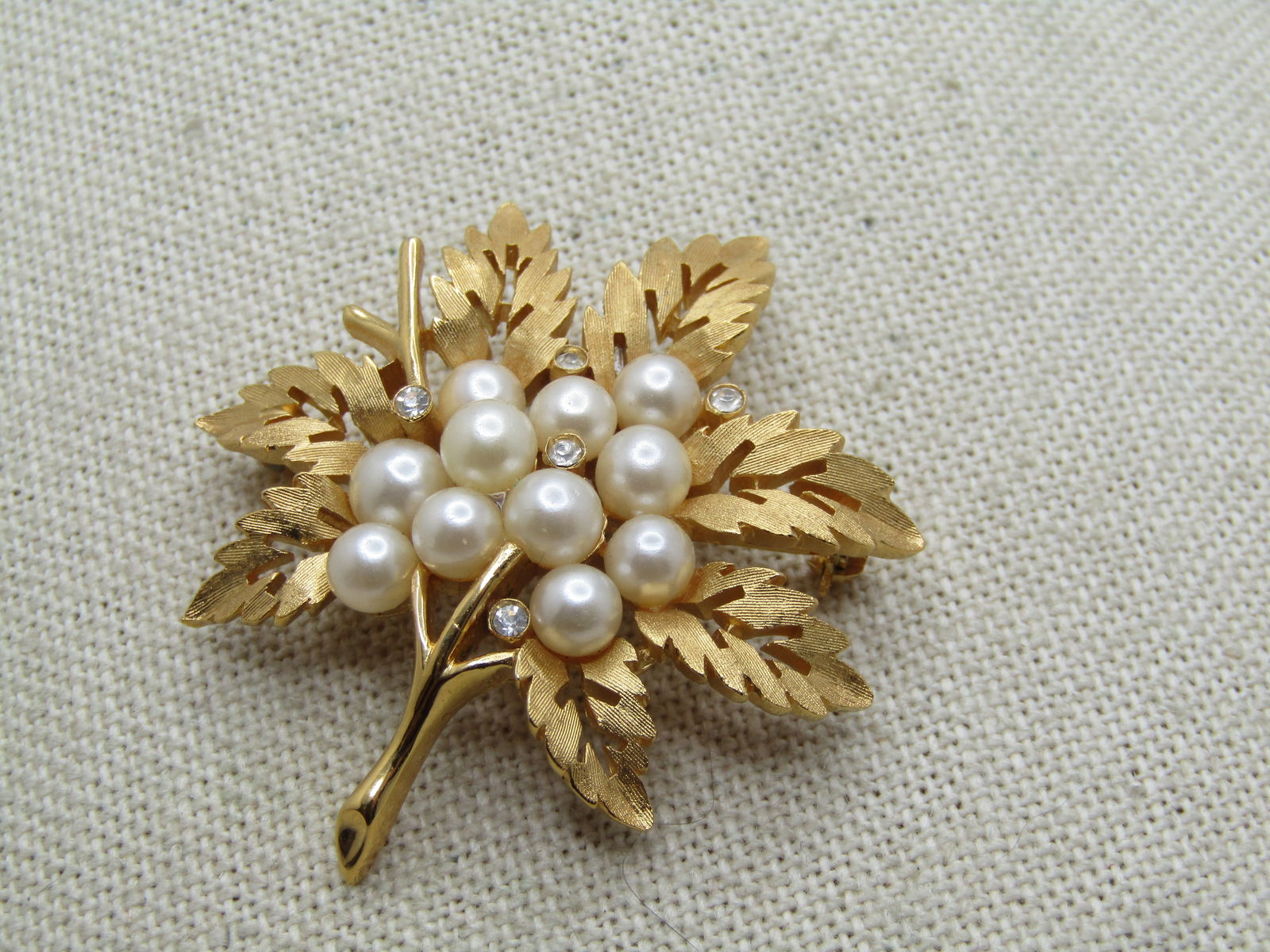 Vintage Faux Pearl Rhinestone Leaf Brooch, Crown Trifari, 1960's.: Vintage Faux Pearl Rhinestone Leaf Brooch, Crown Trifari, 1960's, gold tone, textured finished, cut out design in the curved leaves. The stems are smooth and shiney. The center of the leaf has a clust