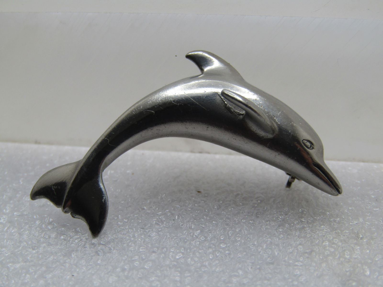 Vintage Curved Dolphin Brooch, 1970's-1980's: Vintage Curved Dolphin Brooch, 1970's-1980's. Silver tone and appx. 1.75" wide and slightly over 1/2" wide at the back tail and widest part of the body. The fins stick up on the back and on the