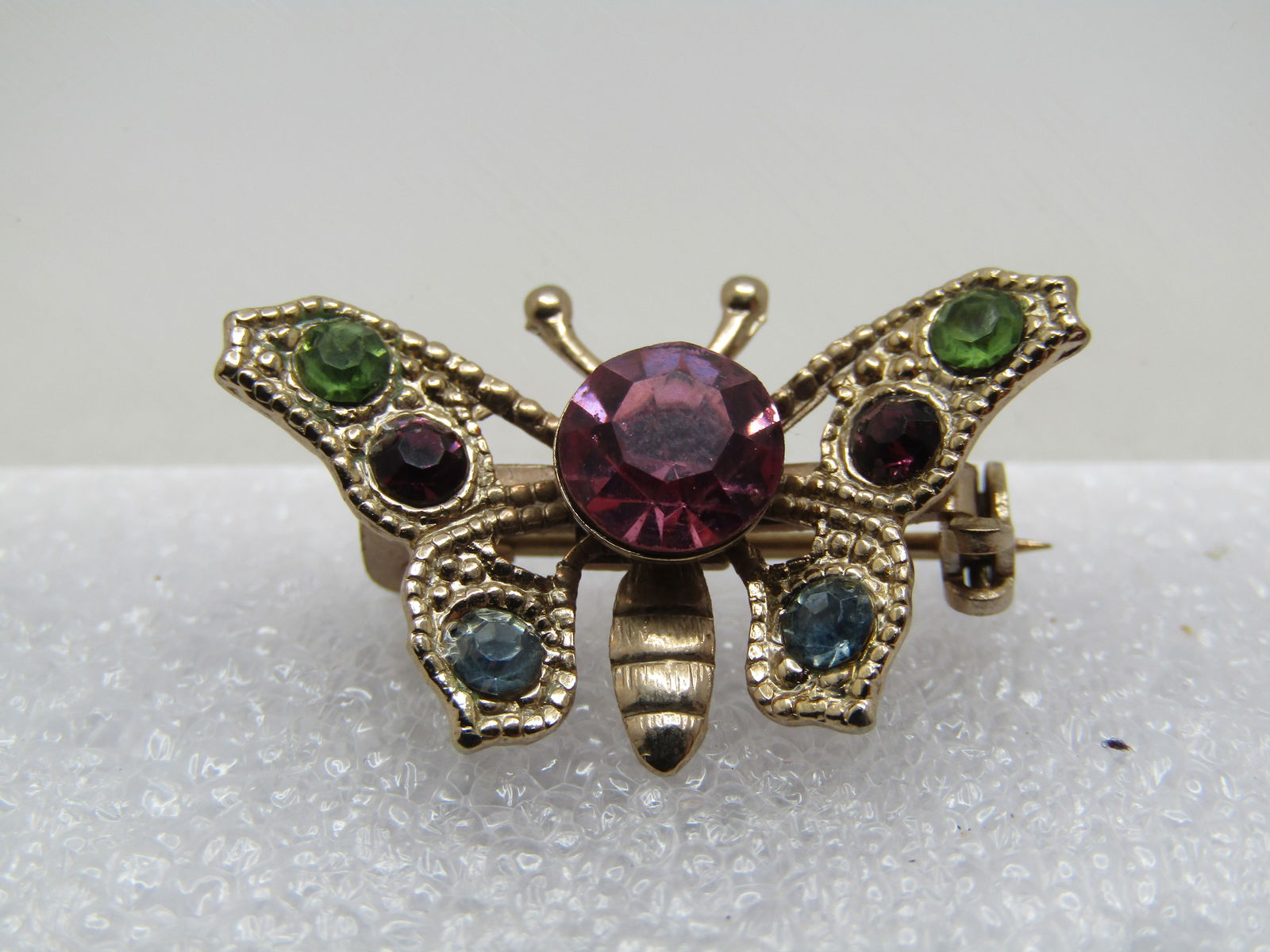 Vintage Rhinestone Butterfly Brooch, 1940's-1950's: Vintage Rhinestone Butterfly Brooch, 1940's-1950's. Textured finish on the gold tone rhinestone with 2.5mm rhinestones set in the wings in green, blue and purple and a large pink rhinetone as the