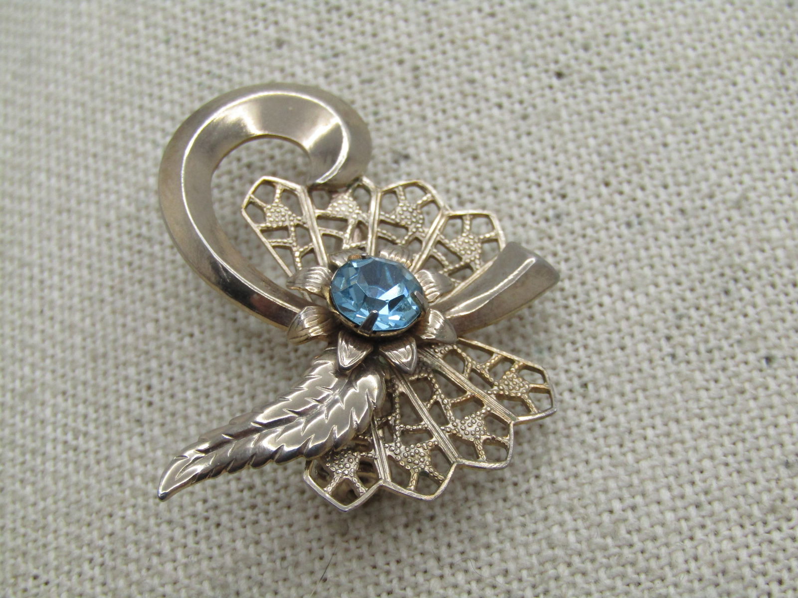 Vintage Filigree Blue Rhinestone Brooch, Leaf And Curl Accent 1960's.: Vintage Filigree Blue Rhinestone Brooch, Leaf And Curl Accent 1960's. Gold tone with filigree fan-like background with raised pearl and leaf accents and a center aqua blue 6.5mm rhinestone. 1" by
