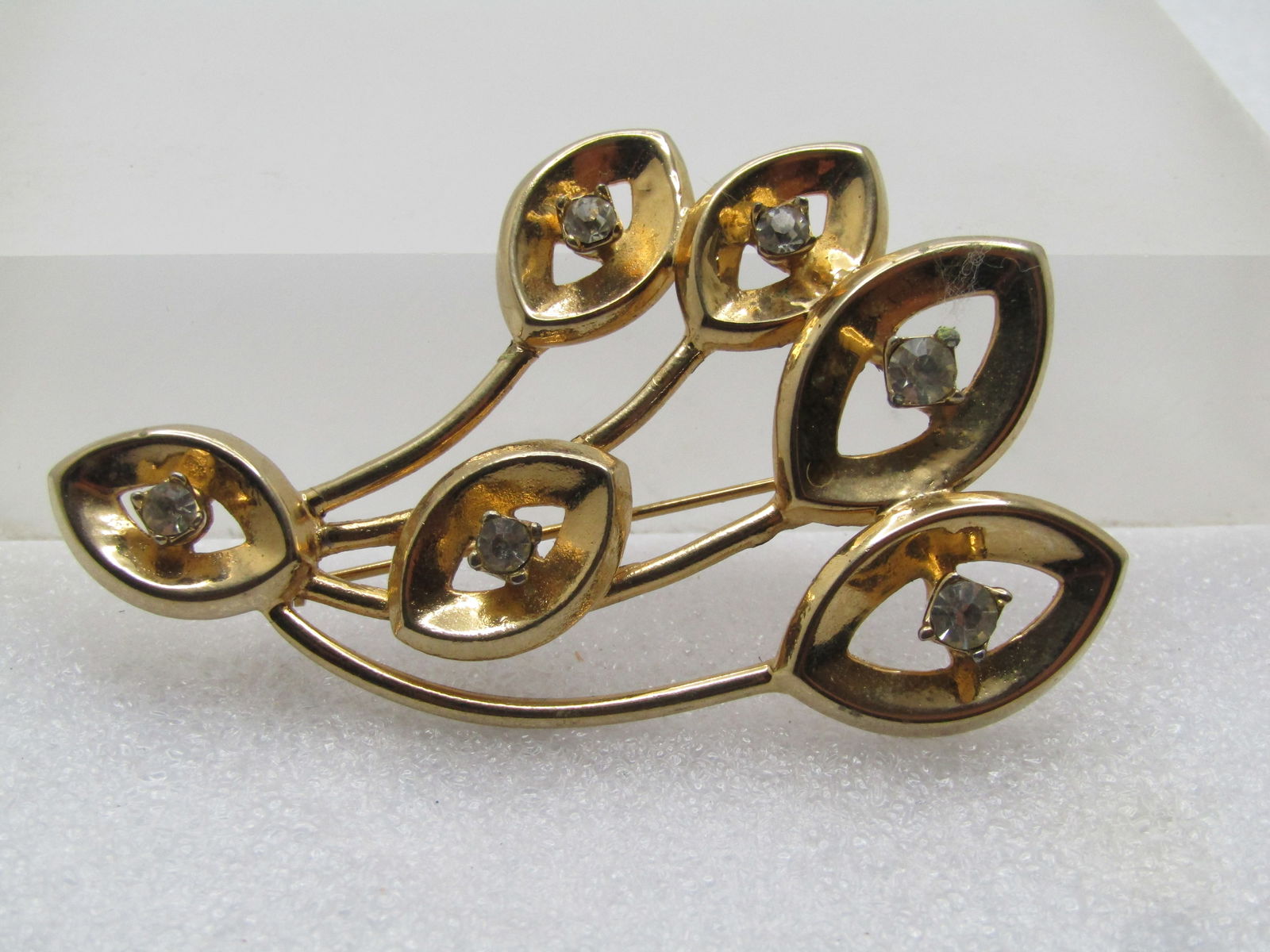 Vintage Mod Leaf Brooch with Rhinestones, 1960's: Vintage Mod Leaf Brooch with Rhinestones, 1960's. It is appx. 2.25" tall by 2" Wide. Curved stems with leaf-shapes with open areas in the center and a clear rhinestone set raised on the center opening