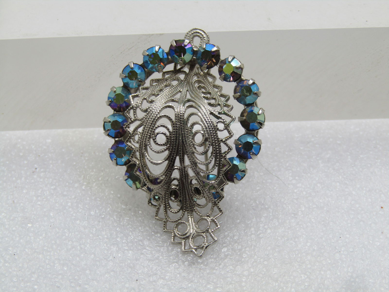 Vintage Blue Aurora Borealis Rhinestone Brooch, Filigree, 1960's: Vintage Blue Aurora Borealis Rhinestone Brooch, Filigree, 1960's. Silver tone with a filigree curled leaf extending beyond both edges and crossing through the center of the brooch. The brooch is appx.