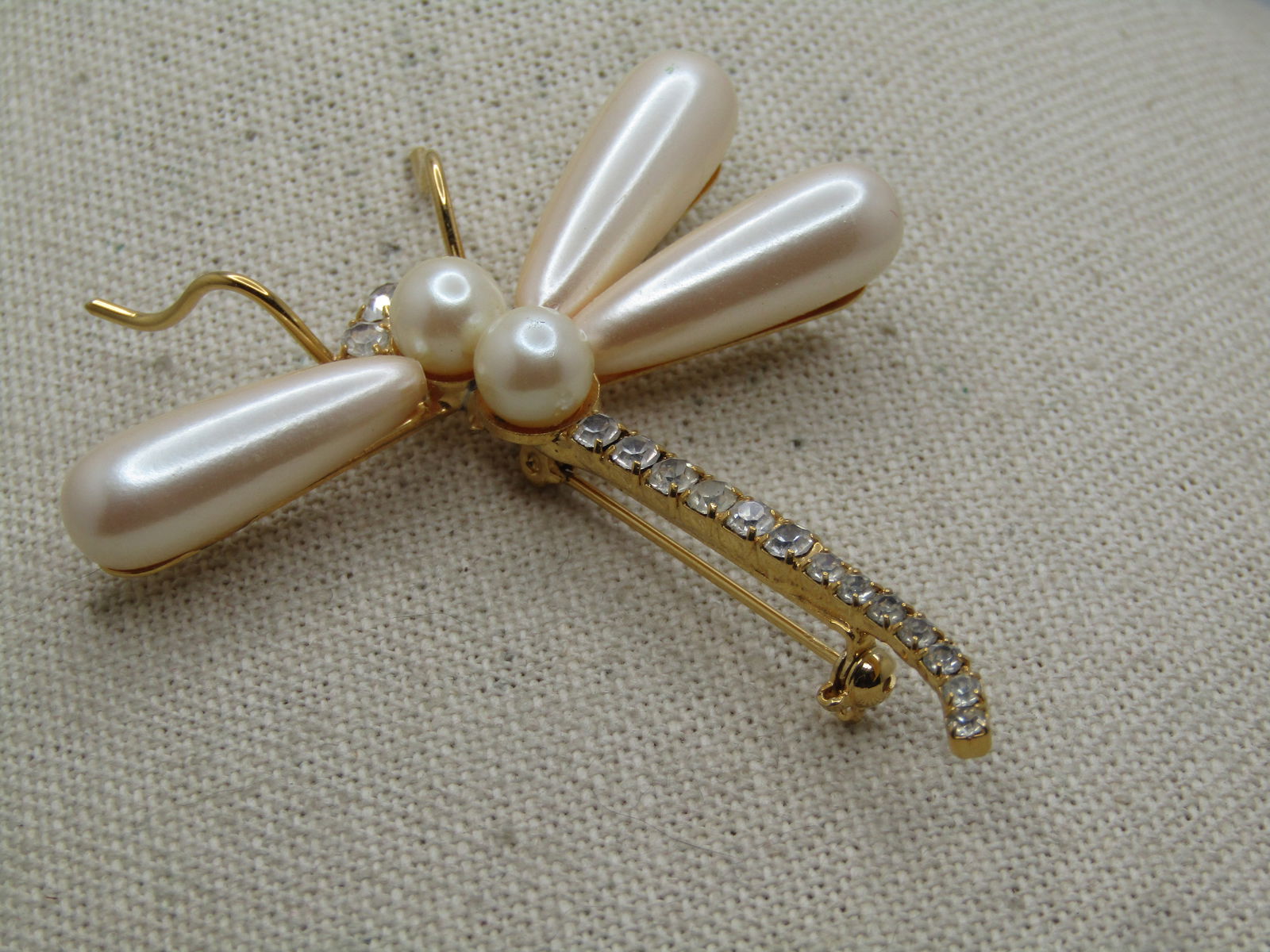 Vintage Rhinestone and Faux Pearl Dragonfly Brooch 1980's.: Vintage Rhinestone and Faux Pearl Dragonfly Brooch 1980's. Gold toned with long faux pearl wings and torso and clear rhinestones through the tail and part of the face. It is not signed or marked by