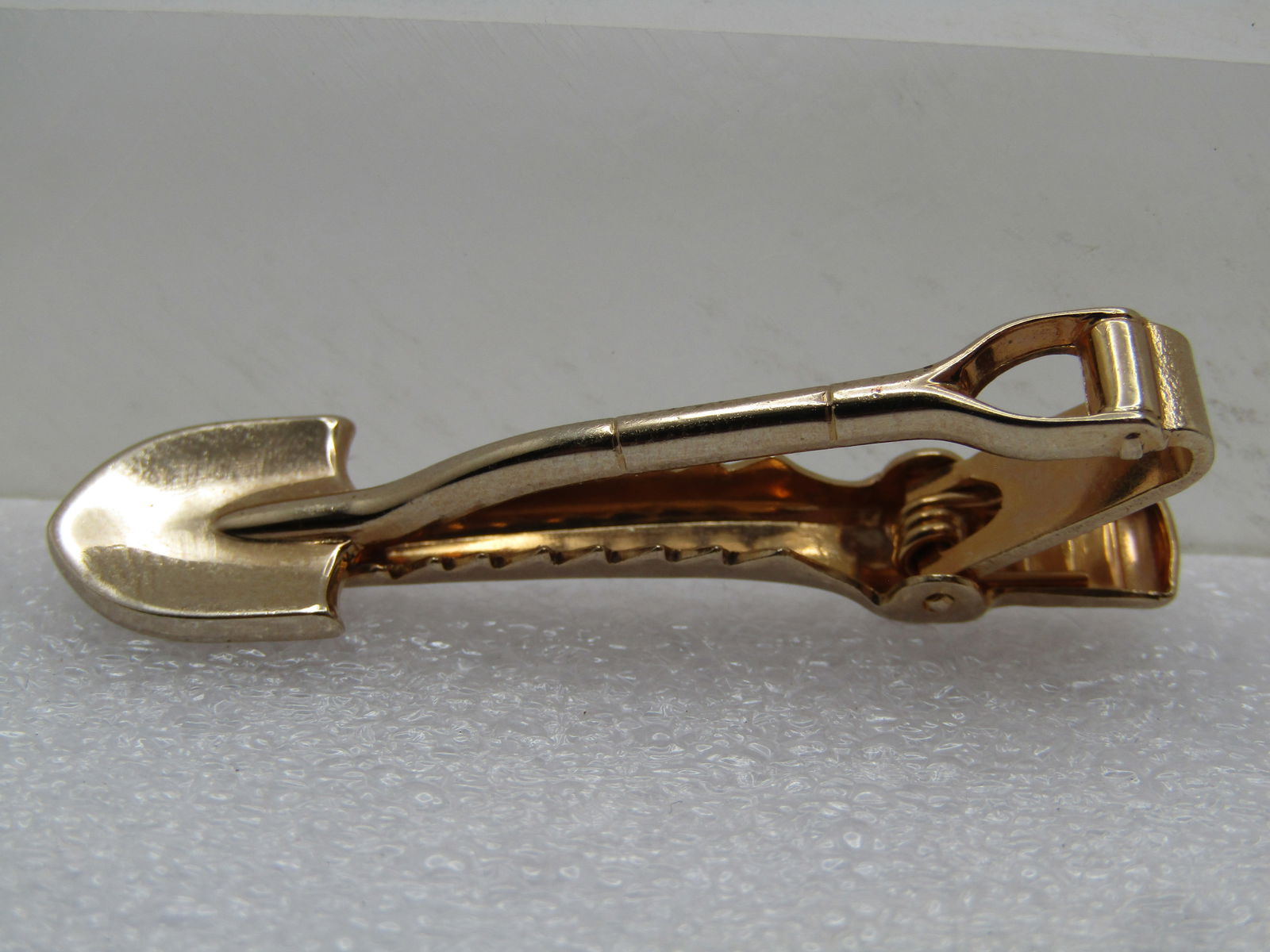 Vintage J.E. Amos Plant Shovel/Spade tie Clasp, Signed Anson, 1960's-1970's: Vintage J.E. Amos Plant Shovel/Spade tie Clasp, Signed Anson, 1960's-1970's. This is gold tone and appx. 1.75" long and 1/2" wide. It is a s hovel on the front and engraved JE Amos Plant on the