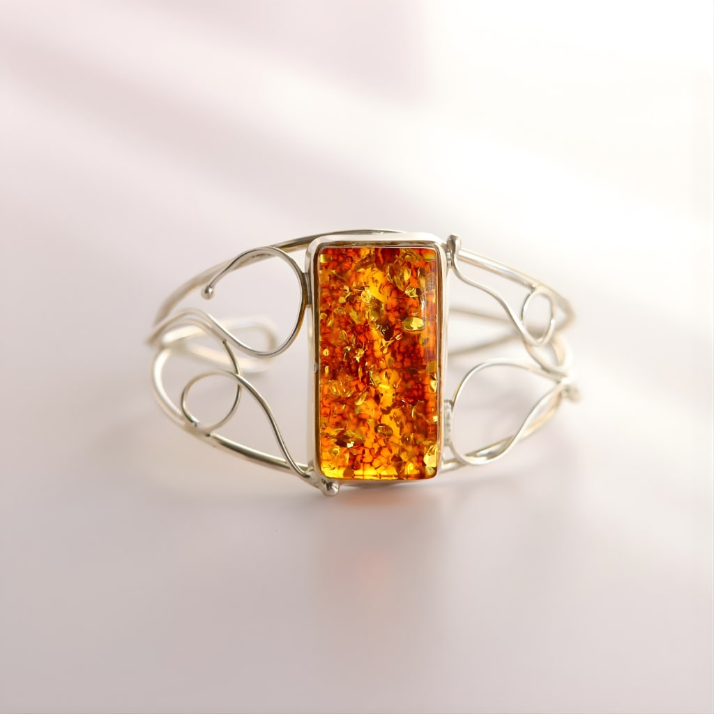 Handmade Baltic Amber Cuff Bracelet: Title:Handmade Baltic Amber Cuff BraceletDescription:This Baltic cognac amber cuff bracelet is crafted with a glowing rectangular gemstone set in 925 sterling silver. The openwork silver frame flows