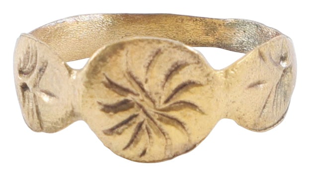 MEDIEVAL WOMAN’S RING C.14TH-15TH CENTURY, SIZE 8 ½: Gilt bronze, size 8 ½. Rounded face band 2.3mm width with foliate engraved expannsions to the shoulders. Circular bezel engraved with a pinwheel motif. Surface textured from burial.